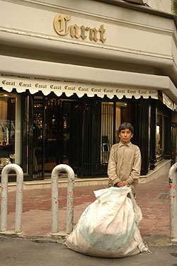 Abdulreza, 12, digs through garbage for recyclable plastics, in front of the exclusive Carat store, northern Tehran. 