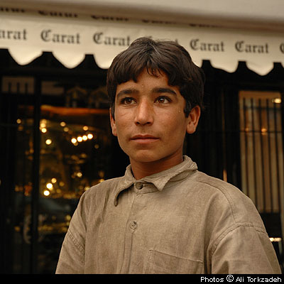 Abdulreza, 12, digs through garbage for recyclable plastics, in front of the exclusive Carat store, northern Tehran. 